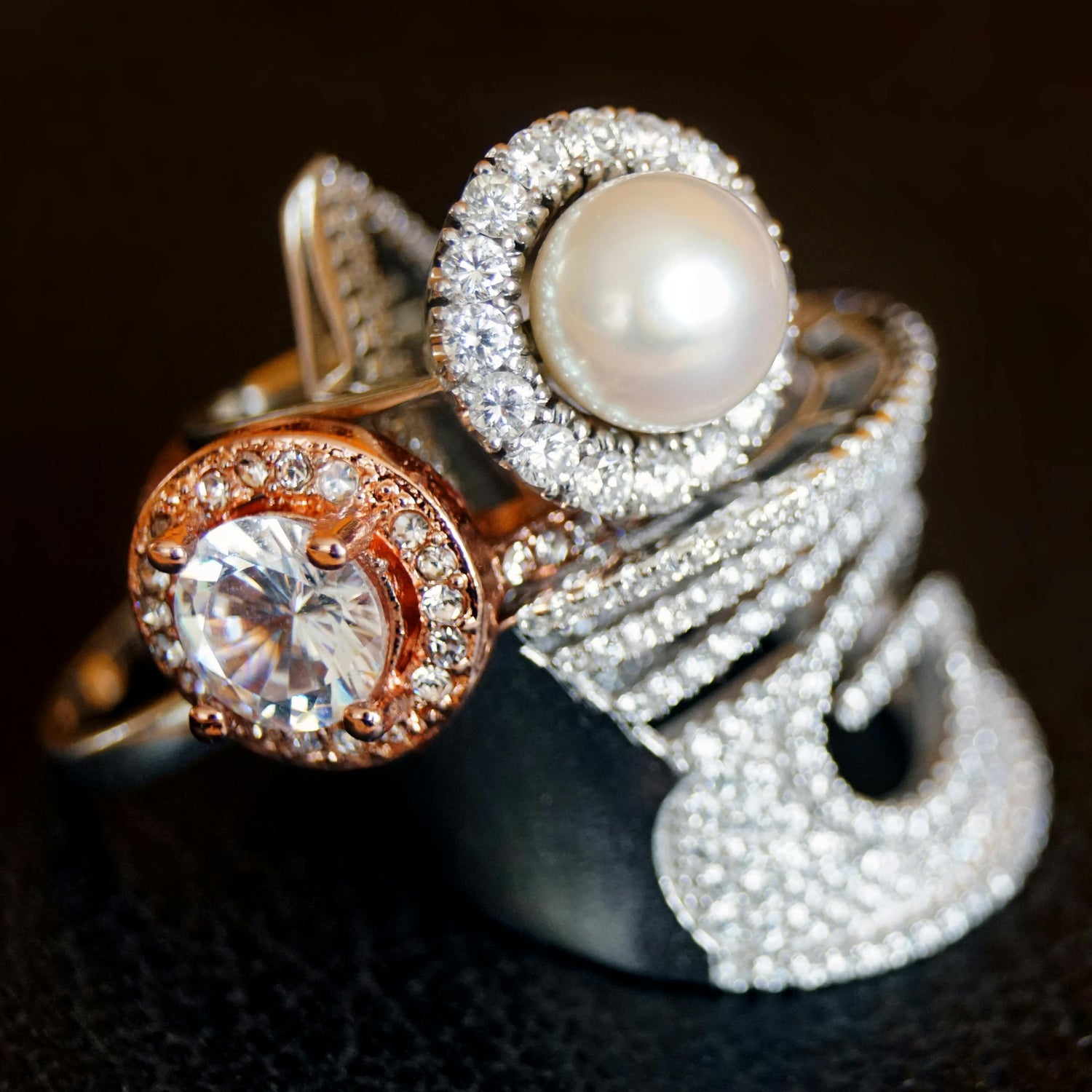 Three rings with pearls and gemstones on a dark background
