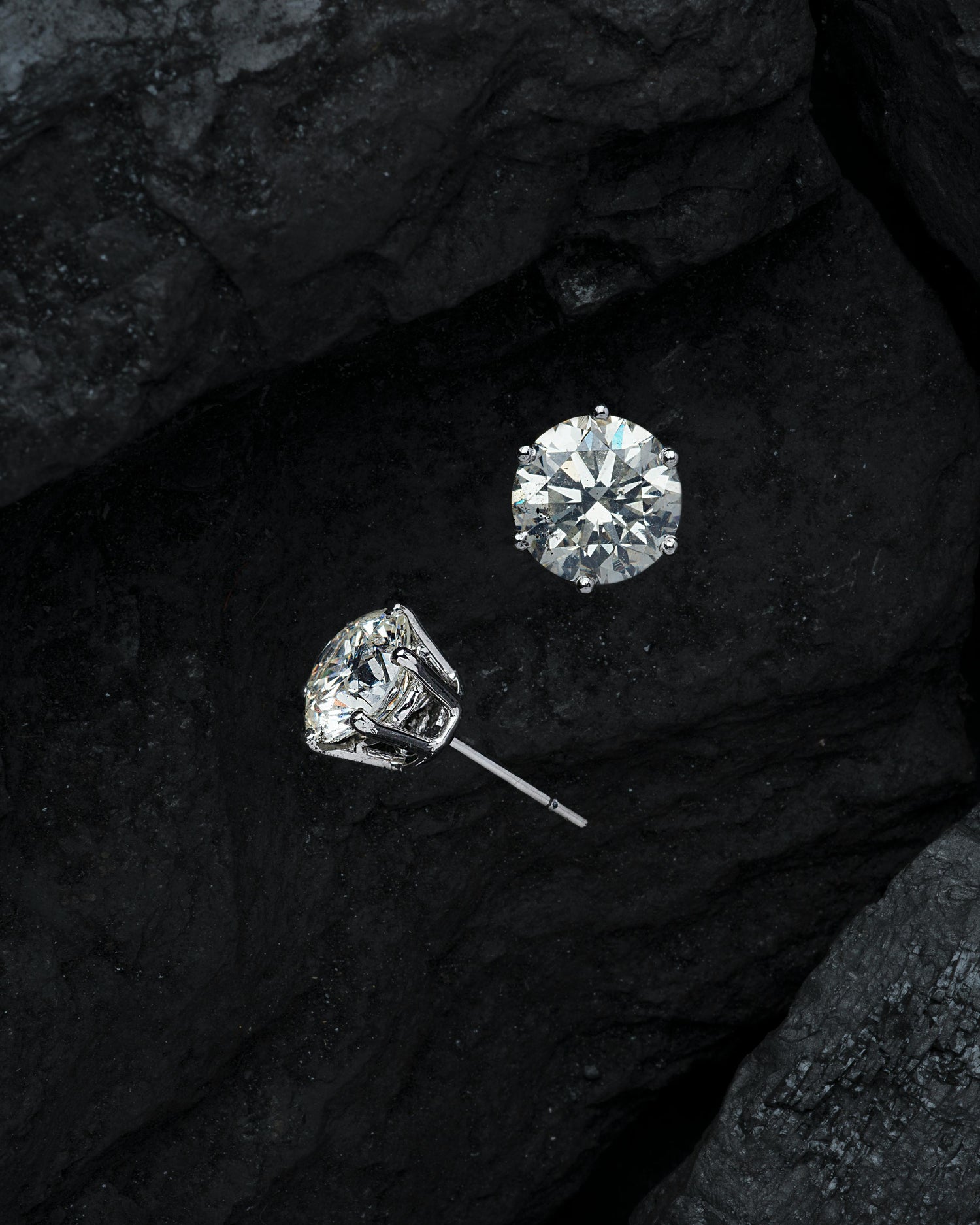 Two diamond earrings on a dark textured surface