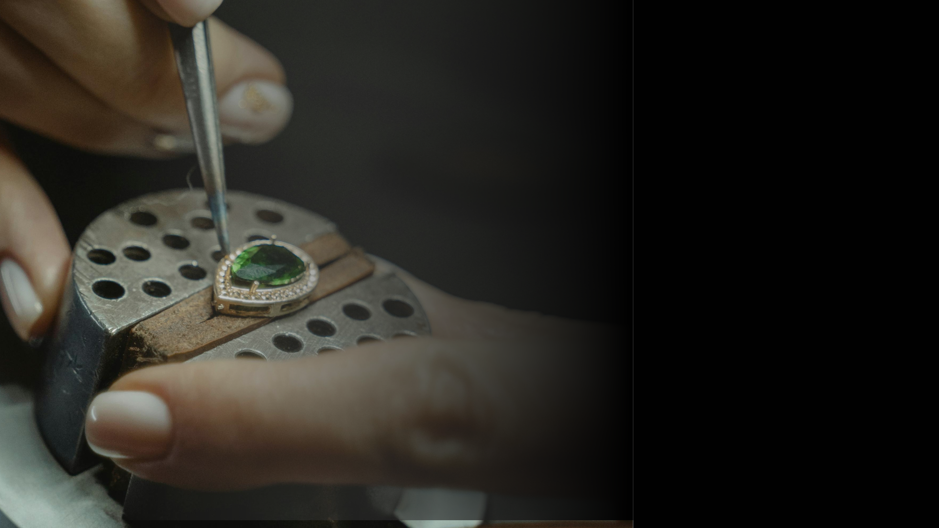 Close-up of a jeweler working on a green gemstone with a tool.